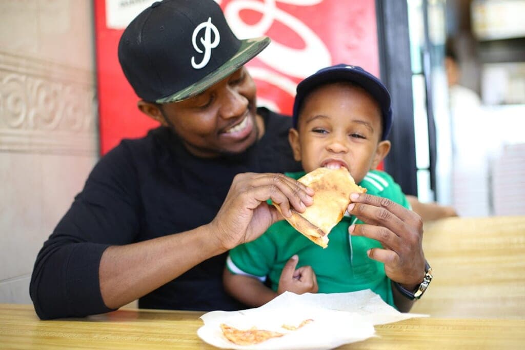 Father feeding toddler pizza