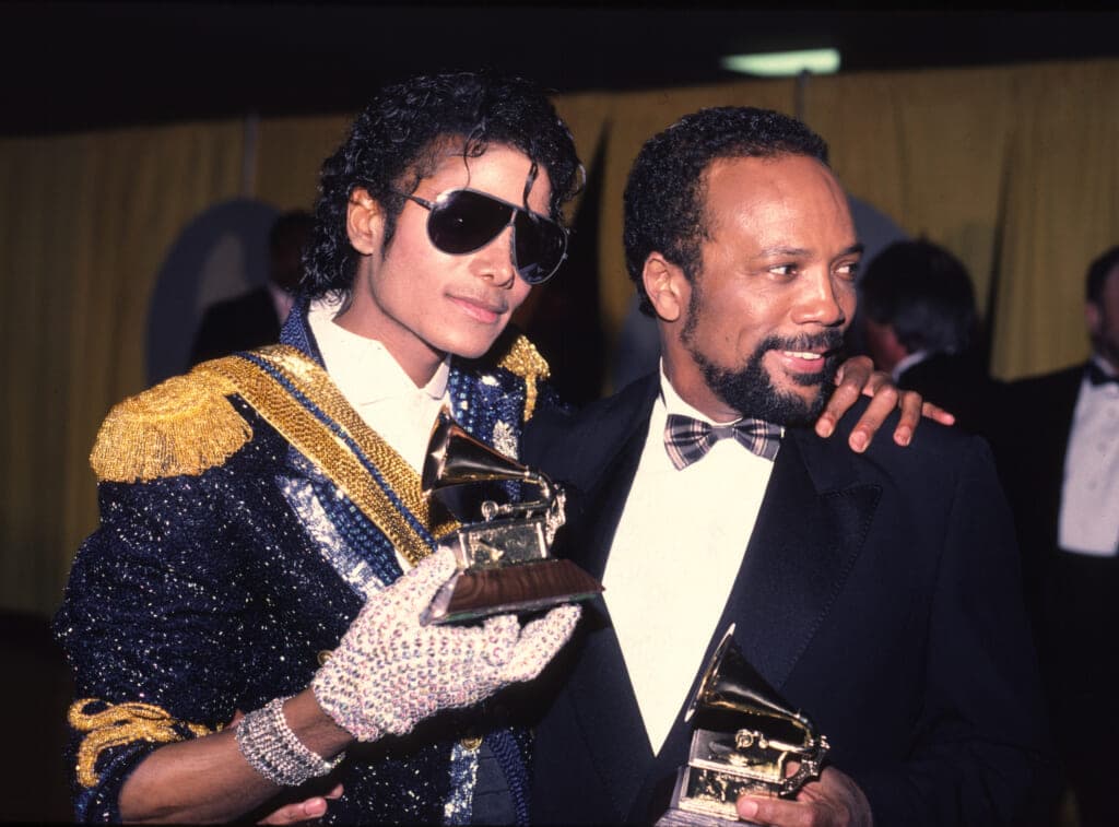 Late singer Michael Jackson holds his Grammy award in his white sequined glove with his arm around producer Quincy Jones