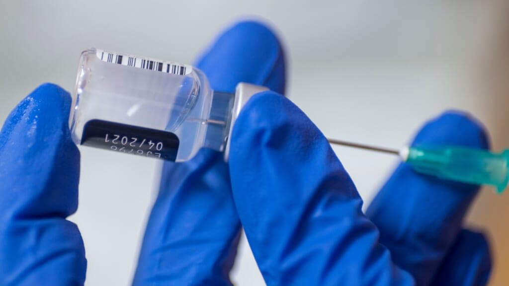Hands in medical gloves put vaccine into a syringe