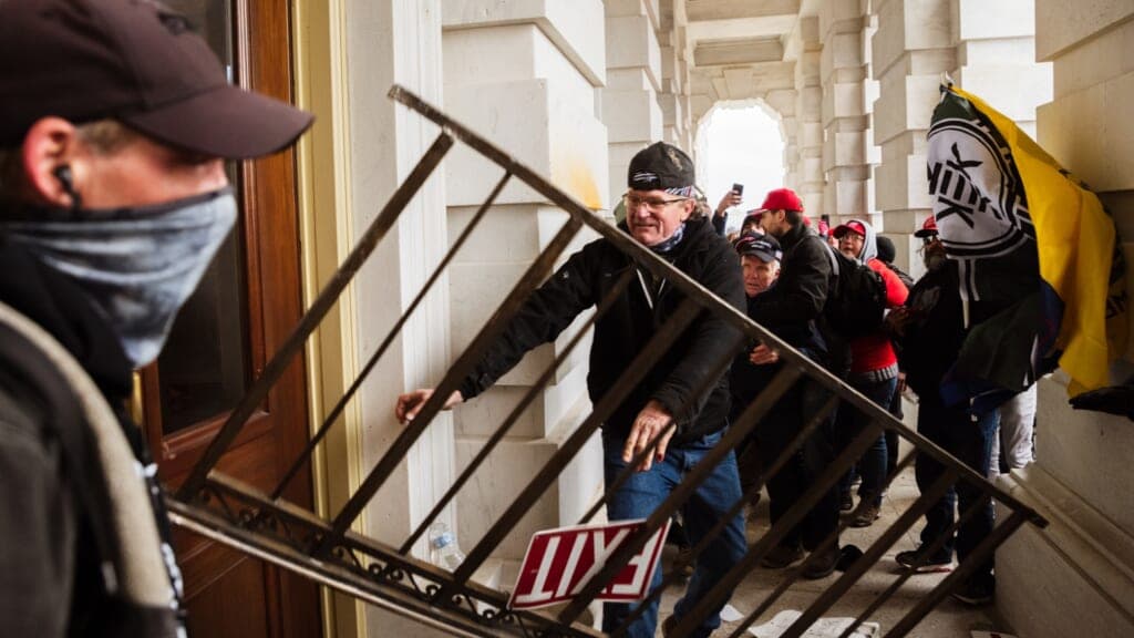 A member of a pro-Trump mob bashes an entrance to the Capitol Building on January 6, 2021