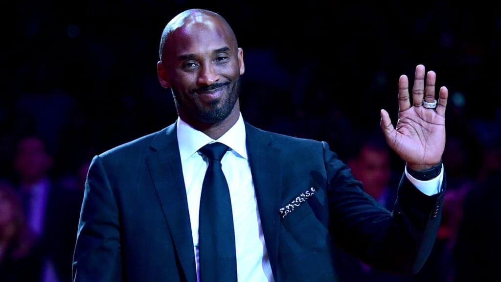 NBA player Kobe Bryant waves, wearing a blue suit and blue tie