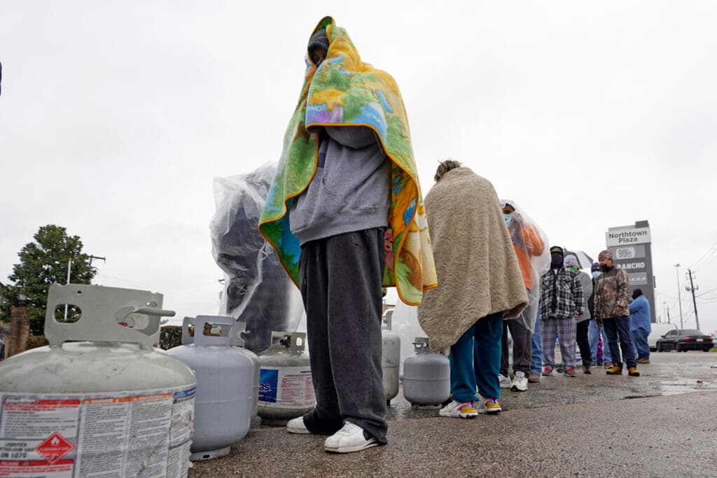 Carlos Mandez waits in line to fill his propane tanks, wearing gray sweats and draped in a colorful blanket
