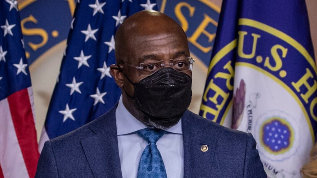 Georgia Senator Raphael Warnock wearing a black face mask, blue jacket and blue tie