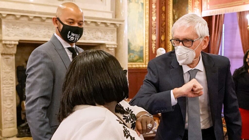 Wisconsin Governor Tony Evers elbow bumps a man as Lieutenant Governor Mandela Barnes looks on