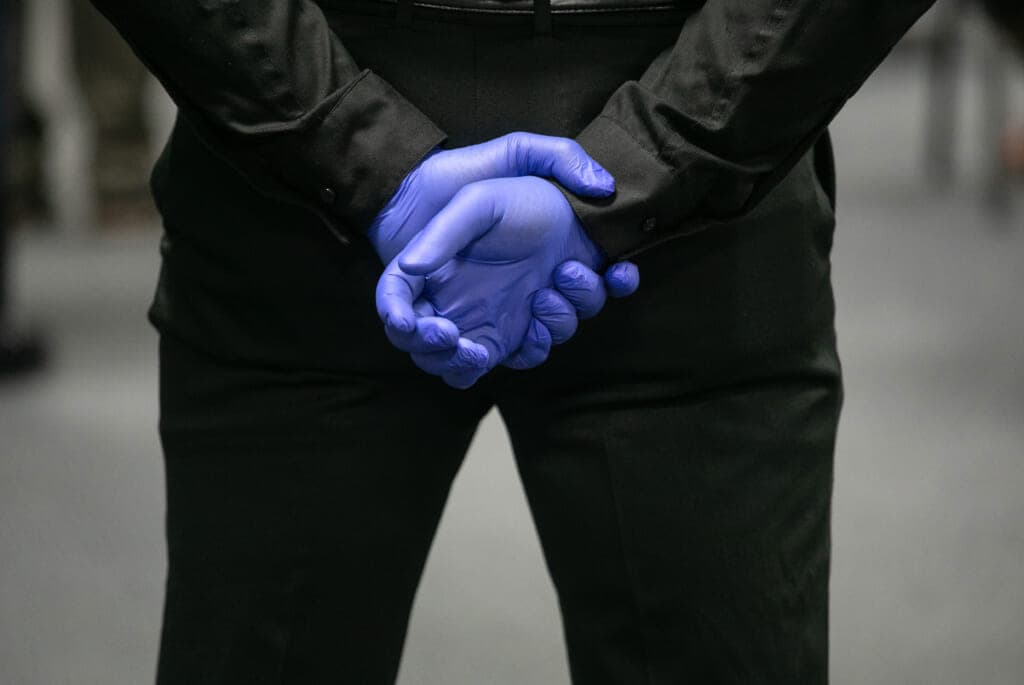 The back of a person in black wearing purple gloves, hands folded