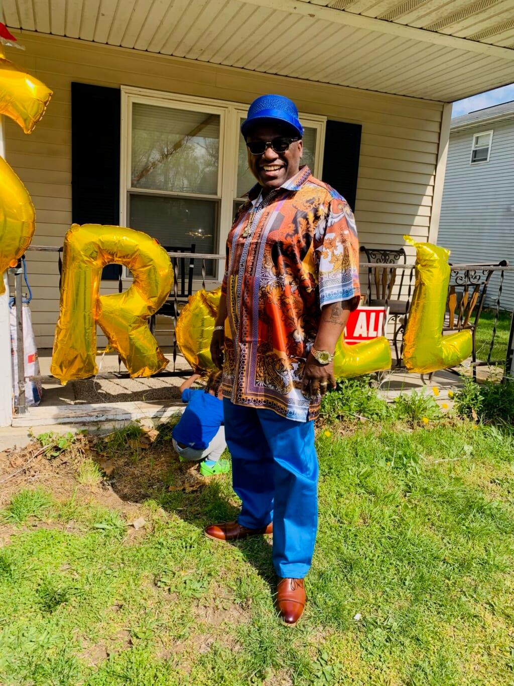 Brian Burnside, recently released from prison, wearing a blue hat, multicolored shirt and blue pants