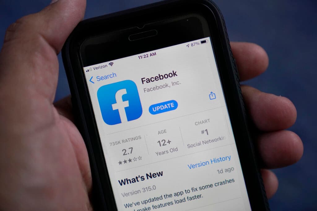 A hand holding a smartphone with the App Store Facebook screen