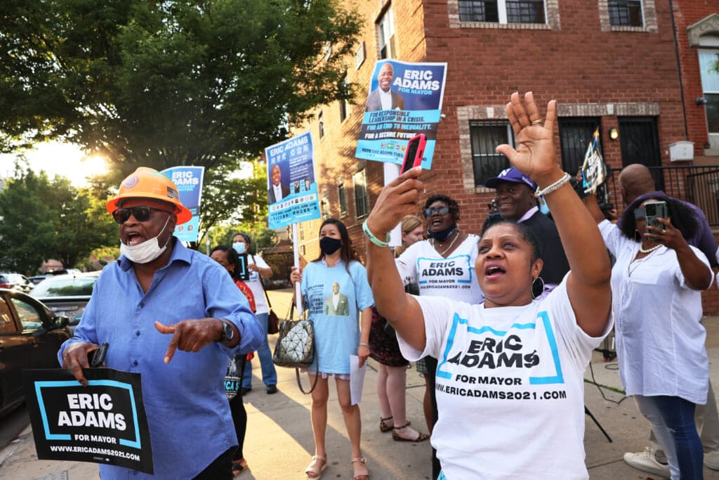 A group of people wear T-shirts and hold signs supporting New York City mayoral candidate Eric Adams
