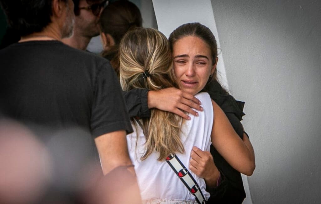 Two women, one in white and one in black, embrace