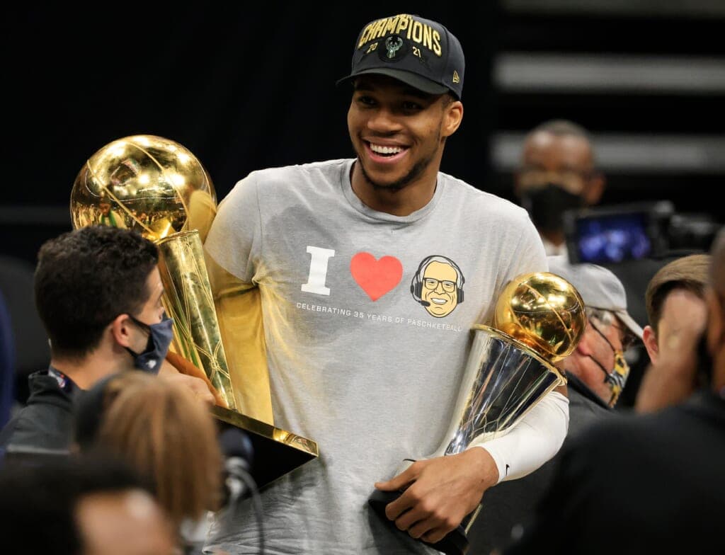 Giannis Antetokounmpo holding his NBA Finals MVP trophy and the Larry O’Brien championship trophy