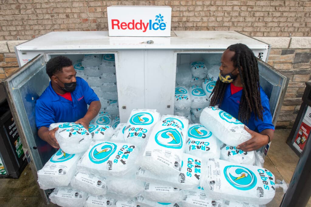 John Smith and Corey Williams of Pelican Ice stack bags of ice into a gas station freezer