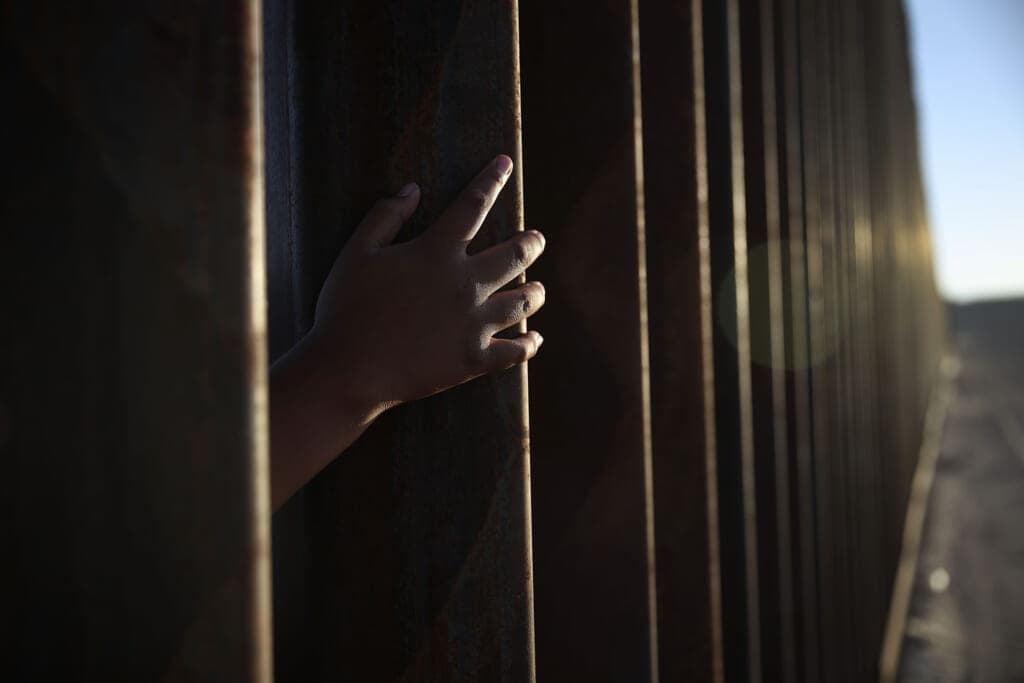 A child reaches through from the Mexican side of the U.S./Mexico border fence