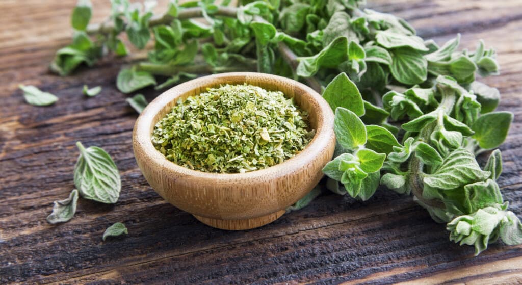 Oregano stalks next to a wooden bowl of chopped oregano