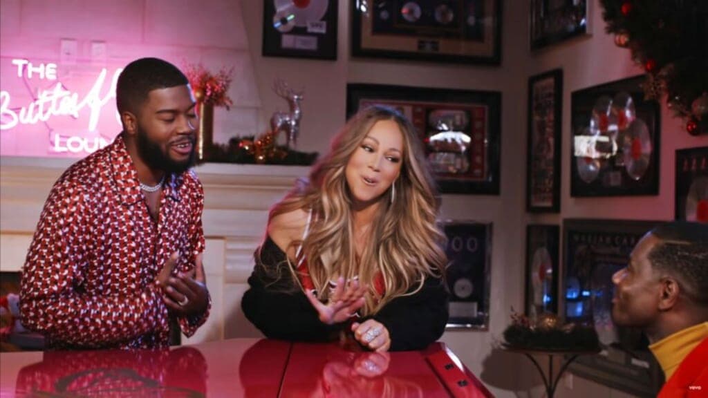 Singers Khalid and Mariah Carey lean on a red piano as they sing