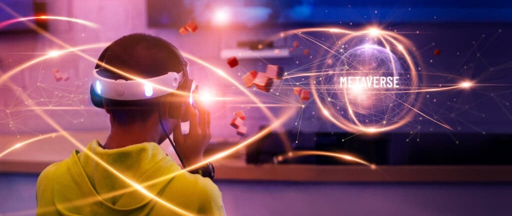A person in virtual reality glasses and a yellow hoodie observes an image of the world reading "Metaverse"
