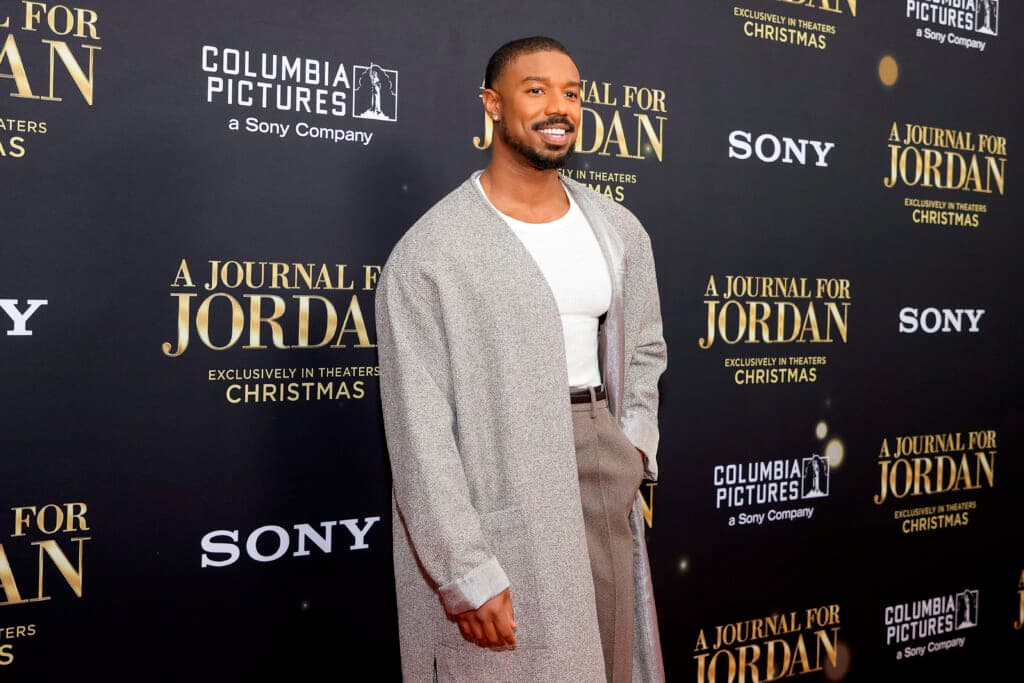 Actor Michael B. Jordan poses wearing a long gray jacket, white shirt and brown slacks