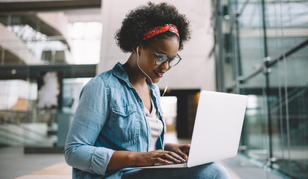 A woman wearing earbuds with a laptop on her lap