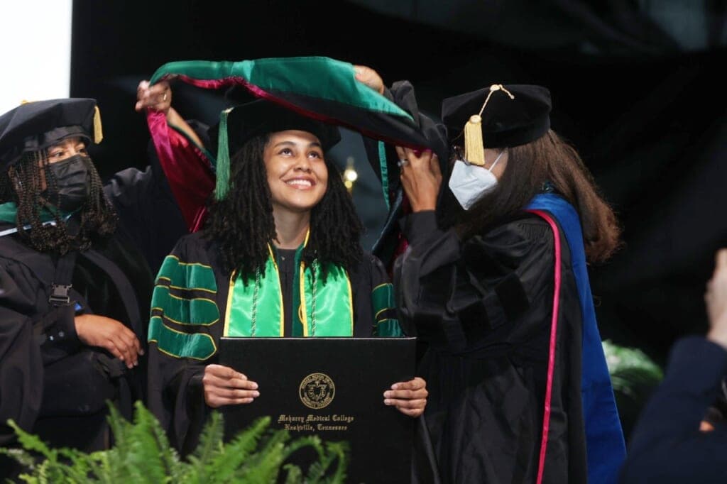 Zindzi Thompson looks up as a green and red sash is placed over her head by two women in black graduate gowns