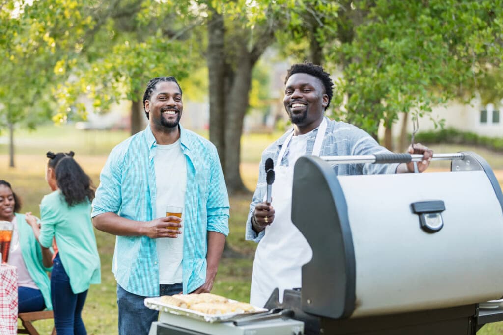Two men smile near a barbecue grill