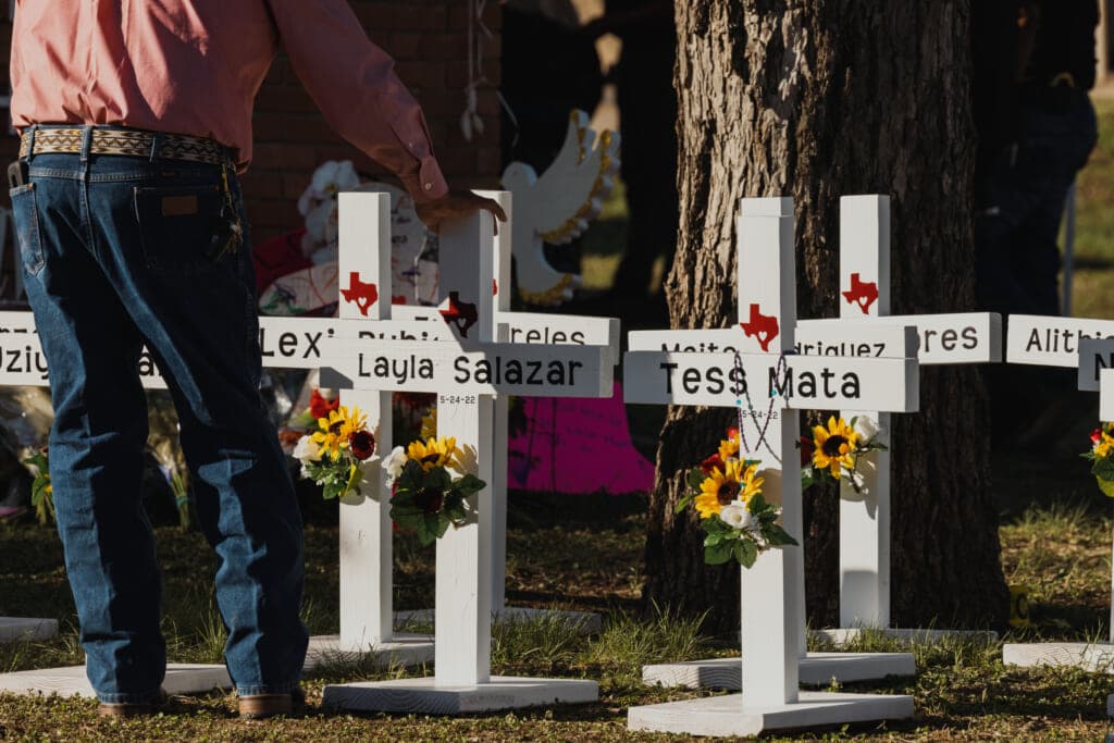 A man places his hand on a cross bearing the names of the victims of a mass shooting