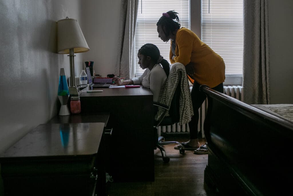 Abigail Previlon sits at a desk using her computer while her mother Carlene leans over her shoulder.