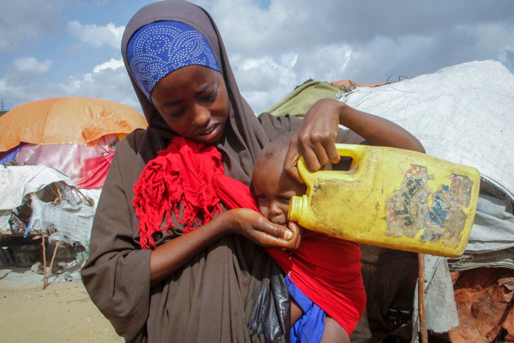 A Somali woman gives water to her baby from a plastic container