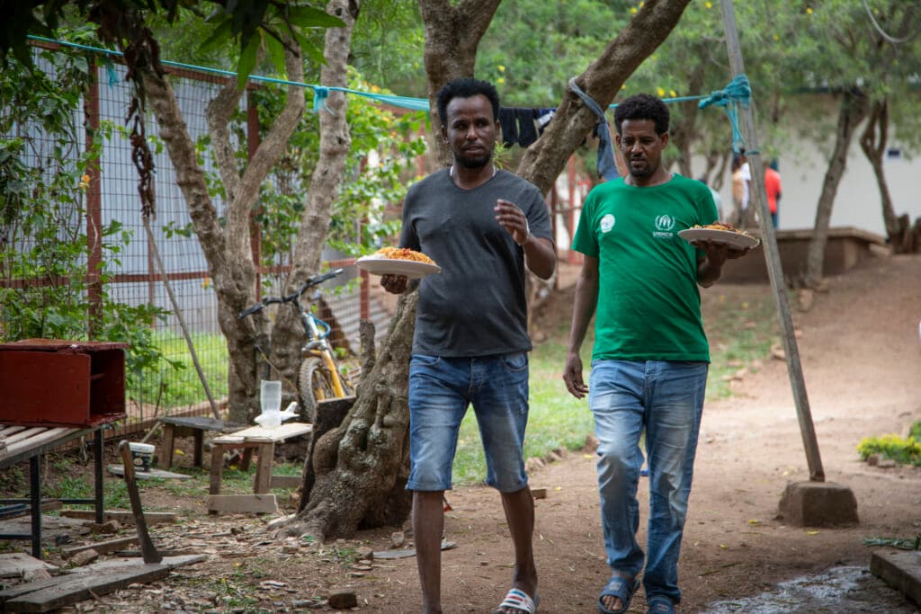 Men who were evacuated from Libya to Rwanda walk with plates of food