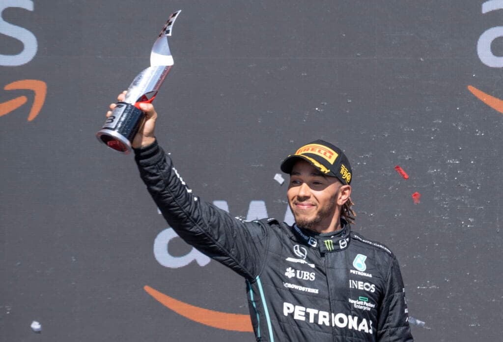Mercedes Team driver Lewis Hamilton of Great Britain, wearing a black racing jacket and baseball cap, holds up a trophy