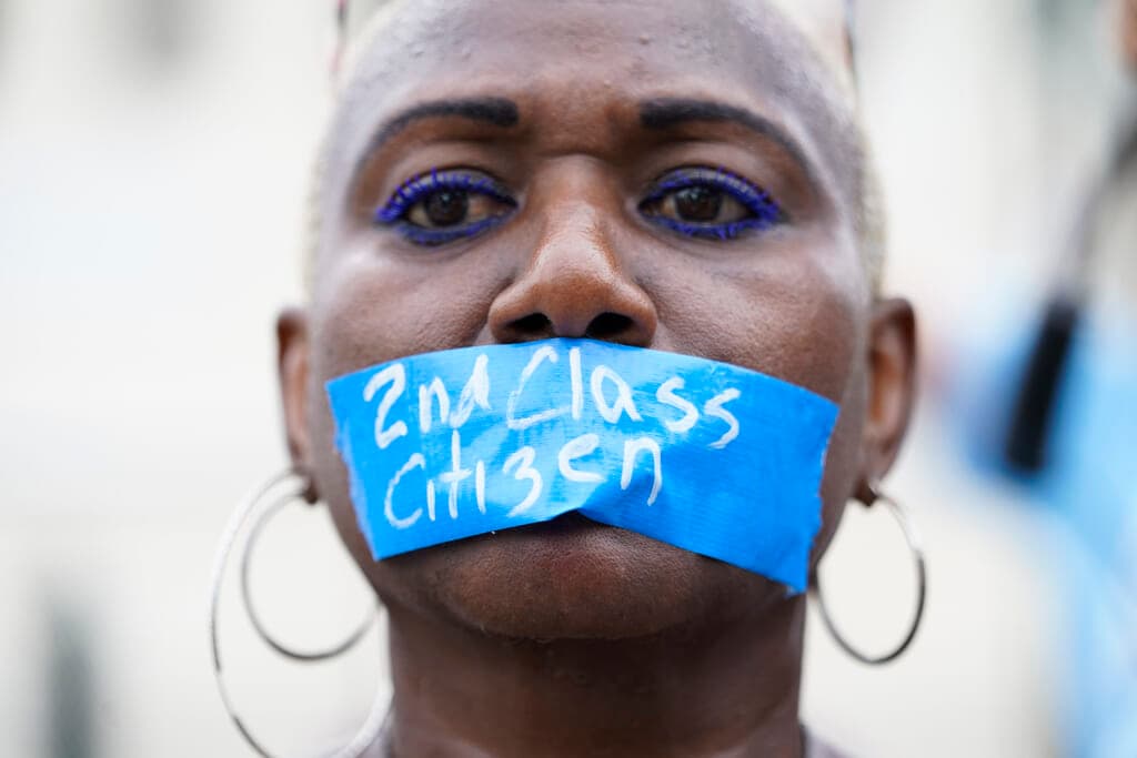 A woman wearing blue tape across her mouth labeled "2nd Class Citizen"
