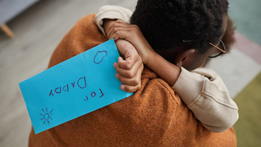 A child hugs their father holding an envelope labeled "For Daddy"