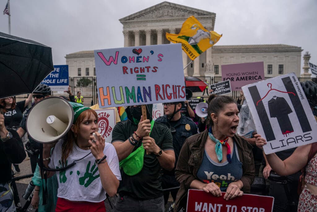 Abortion-rights activistis protest in front of the Supreme Court building, holding signs and a bullhorn