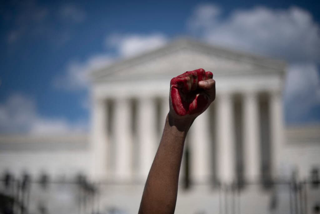 An abortion rights demonstrator raises a fist, painted in red