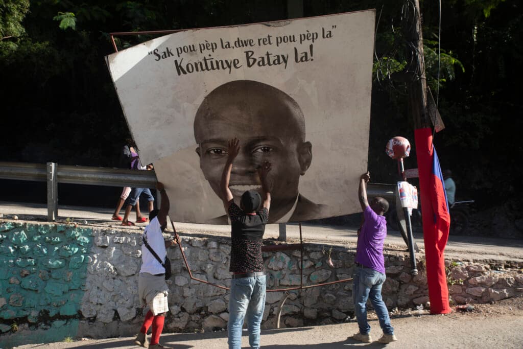 Three people raise a sign portraying slain Haitian President Jovenel Moise