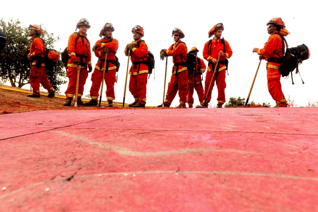 Inmate firefighters in bright orange fire gear prepare to take on the River Fire