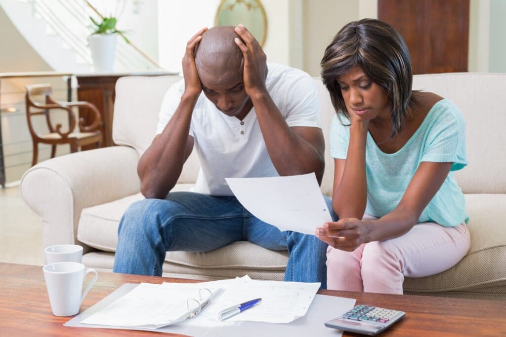 A man holds his head in his hands as a woman looks at paperwork