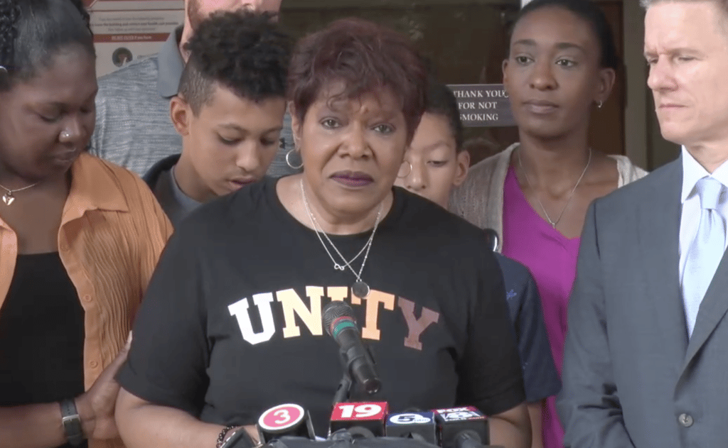 Pam Walker, wearing a black shirt reading "Unity," stands at the microphone to speak about her son, Jayland Walker