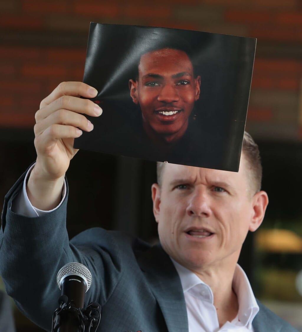 Attorney Bobby DiCello, wearing a white shirt and gray jacket, holds up a photograph of Jayland Walker