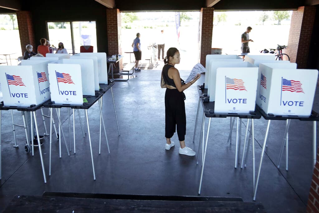A woman holds a ballot while standing among voting machines wearing a black crop top and pants