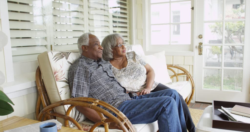 An older couple sits together on a porch loveseat