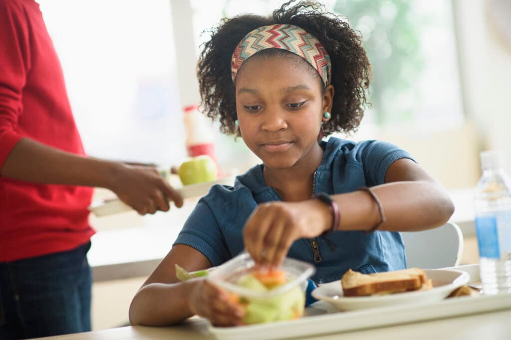 A girl takes fruit from a container on her cafeteria tray