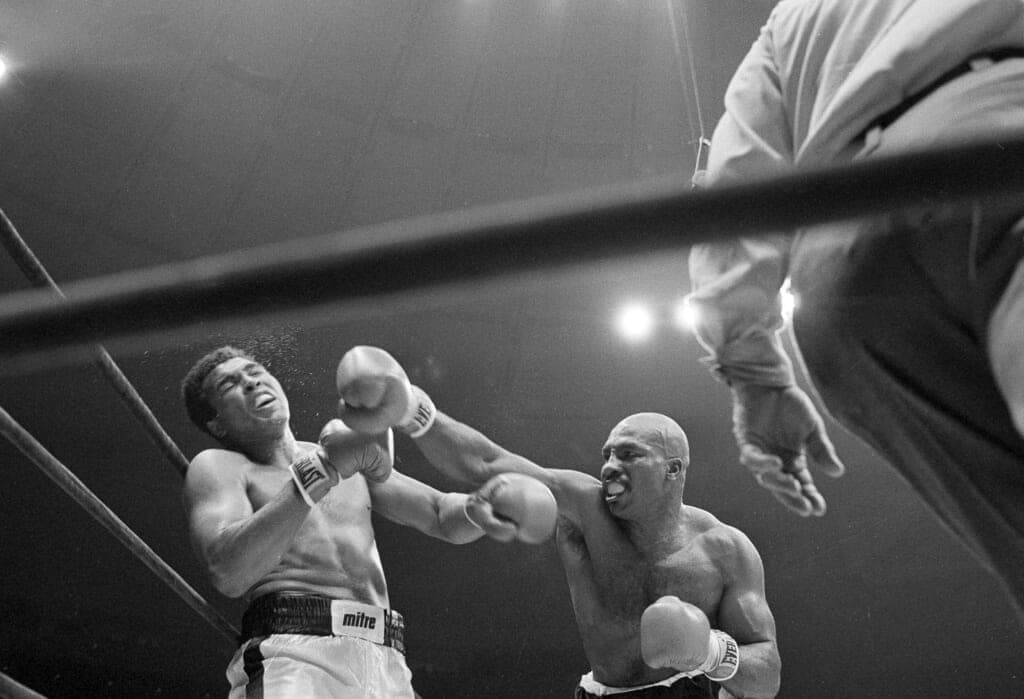 Black-and-white photo of boxer Muhammad Ali being punched by boxer Earnie Shavers in 1977