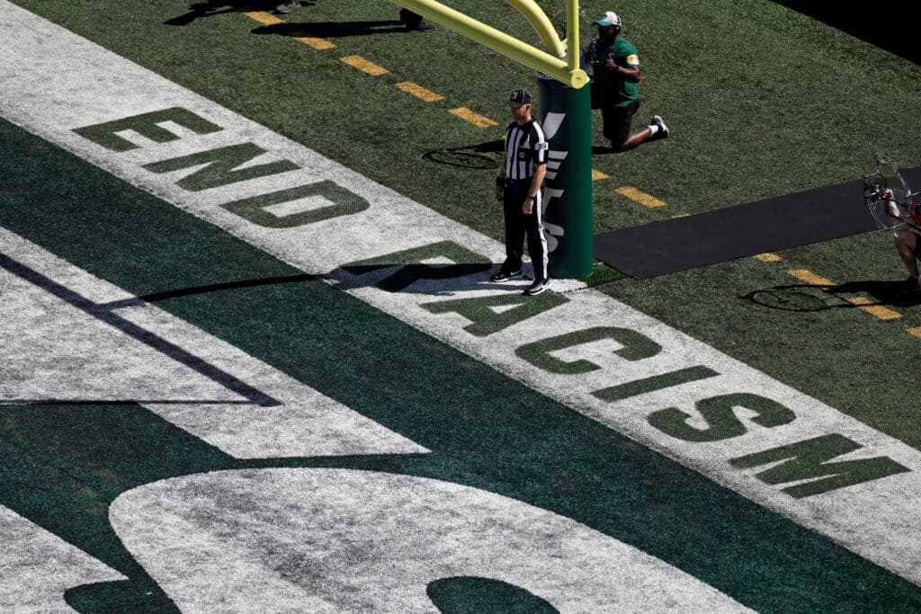 Back judge Rich Martinez stands in the end zone next to the social justice message “End Racism”