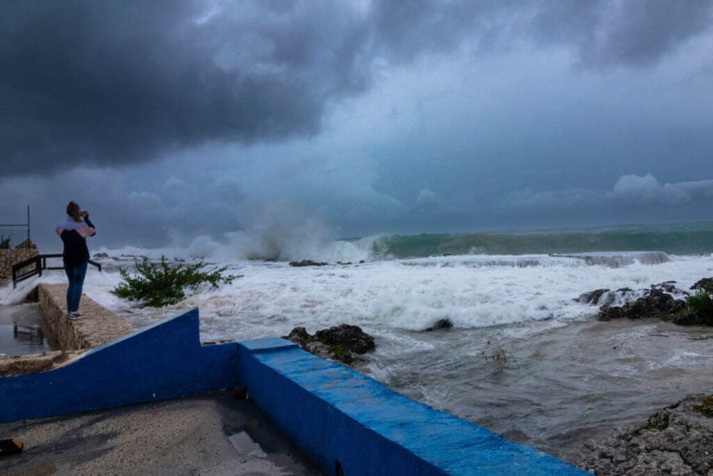 A woman takes photos while waves crash against a seawall as Hurricane Ian passes
