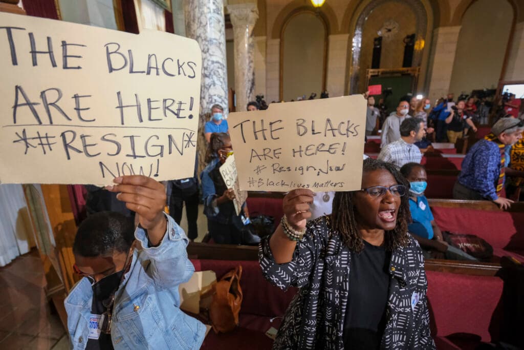 People hold signs and shout slogans before the start the Los Angeles City Council meeting