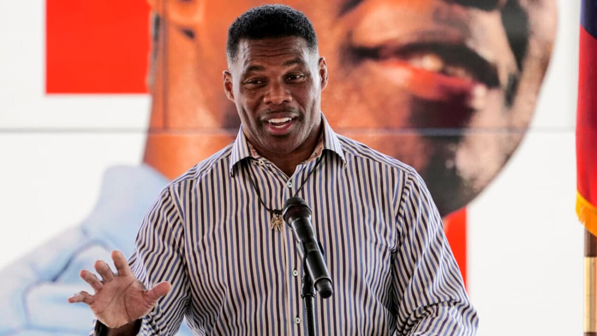 Republican candidate for U.S. Senate Herschel Walker wearing a brown-and-blue striped shirt stands behind a microphone