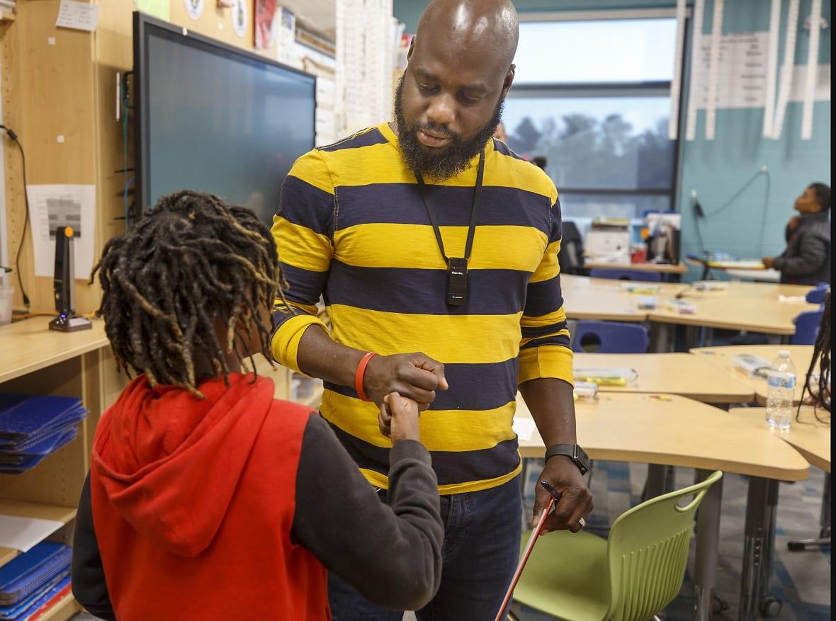 Educator Tyler Wright, wearing a yelllow-and-gray striped top, fist-bumps a child in a red and black hoodie