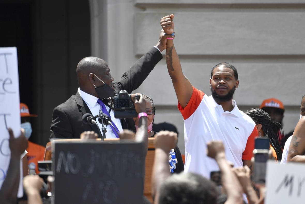Attorney Benjamin Crump holds up the hand of Kenneth Walker during a rally