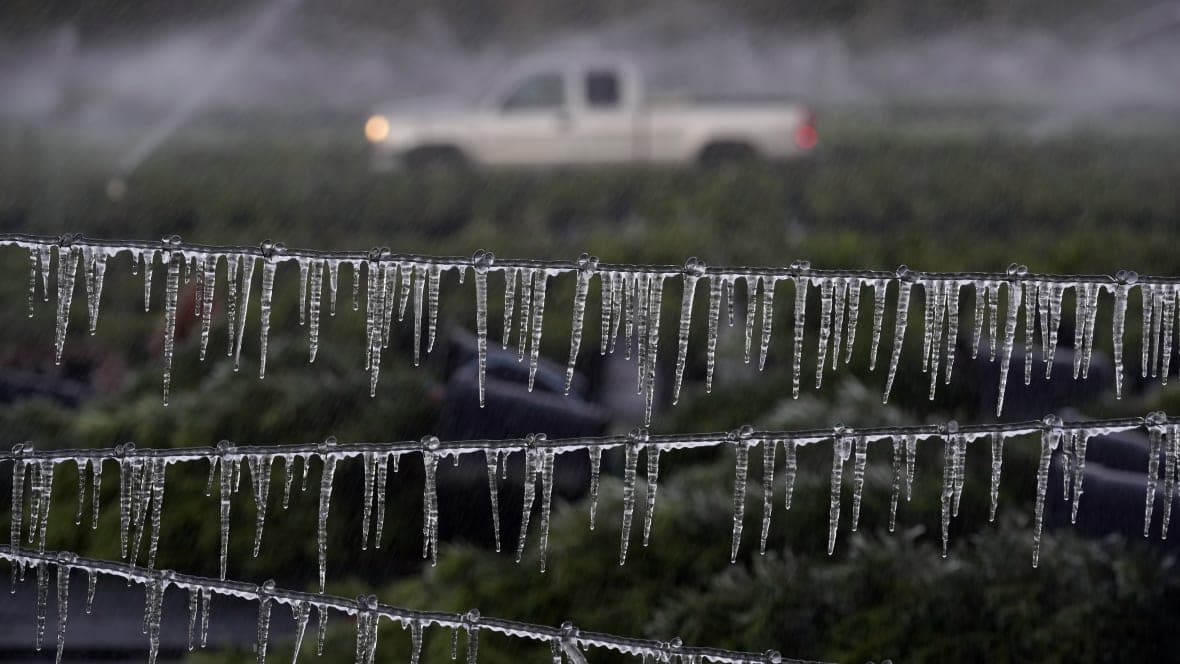 A farmer drives by an icicle-covered fence