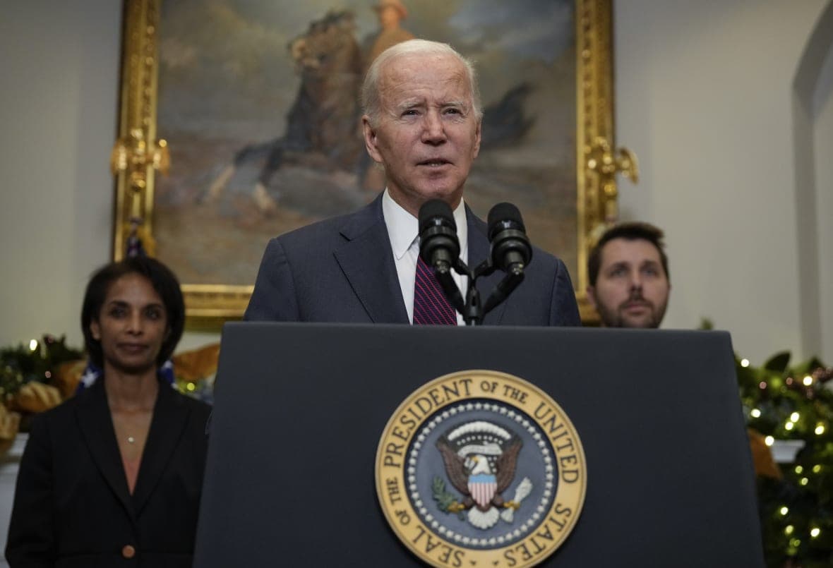 President Joe Biden, wearing a  gray suit, white shirt and red-and-black striped tie, stands at a podium