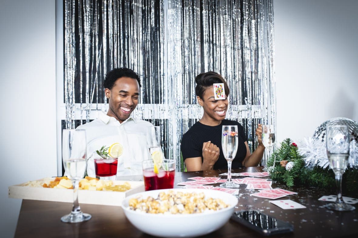 A couple at a dining table with playing cards in front of them and a card on the woman's forehead